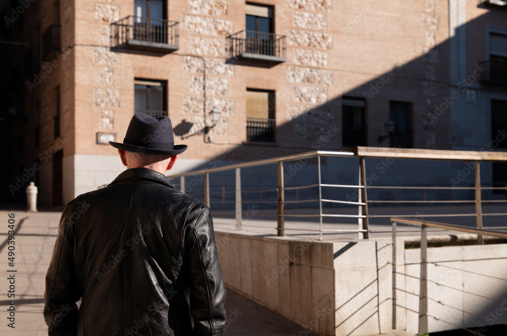 Rear view of adult man in hat and leather jacket on street. Madrid, Spain