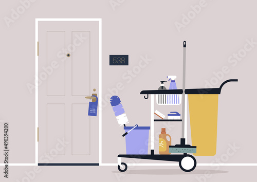 A hotel room service cart with cleaning tools and detergents, a mop, a feather duster, and washing chemical liquids in bottles