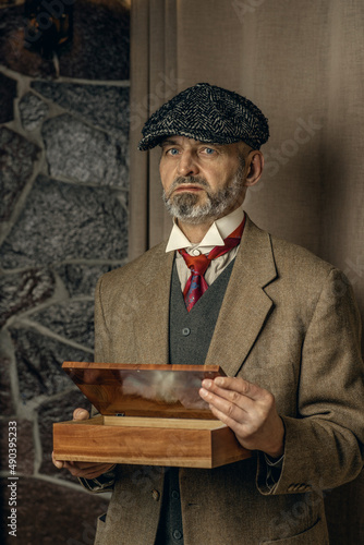 An adult man in a suit and cap holds a wooden box, dressed in the style of Peaky Blinders