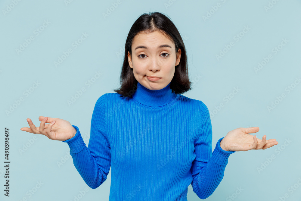 Frustrated young woman of Asian ethnicity 20s years old wears blue shirt spreading hands shrugging shoulders have no idea nothing to say isolated on plain pastel light blue background studio portrait. Frustrated young woman of Asian ethnicity 20s years old wears blue shirt spreading hands shrugging shoulders have no idea nothing to say isolated on plain pastel light blue background studio portrait.