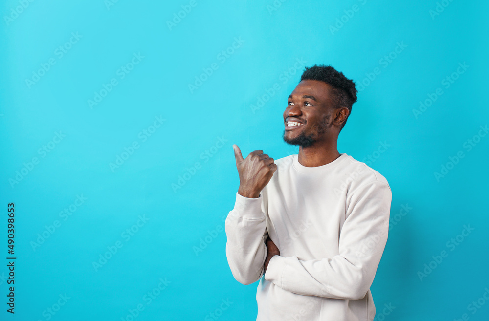 A surprised African student pointing his finger to the side at the copy space on a blue background A surprised African student pointing his finger to the side at the copy space on a blue background