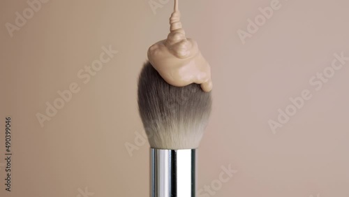 The foundation is poured onto the makeup brush. Decorative cosmetics advertising concept. Brush on a beige background. photo