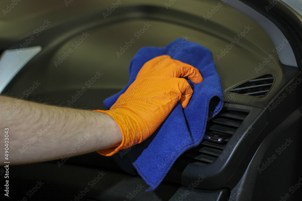 Detailing and car cleaning services,the concept of car washing and cleaning.A male worker in orange rubber gloves,cleaning the plastic of the car interior with a blue microfiber towel.Auto detailing.