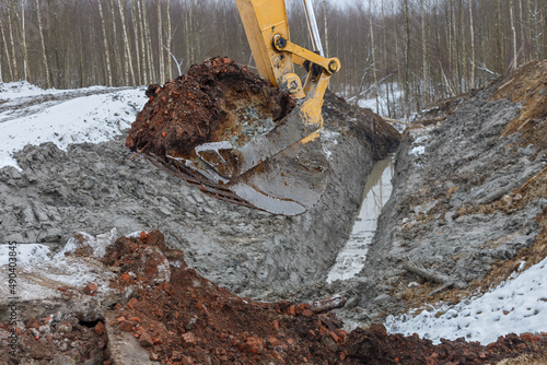 the process of loosening frozen winter soil with an excavator bucket