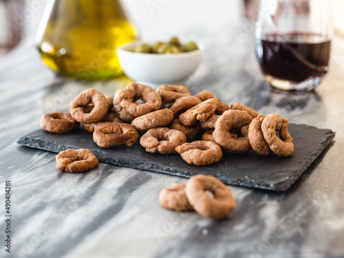 Taralli with red wine on a black slate plate, on a marble table. Vegan aperitif. Red wine, olive oil and olives in the background