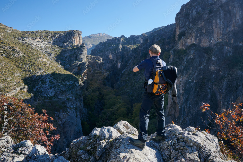 Obraz premium A rear view of a Caucasian male traveler standing on rocks taking picture of the rocky cliffs