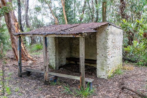 Photograph of an old and damaged white stone shelter in a forest