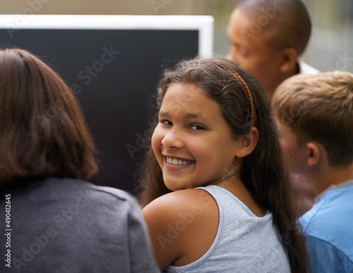 Smiling during computer class. Portrait of a young schoolgirl looking back while working on a computer with her friends.