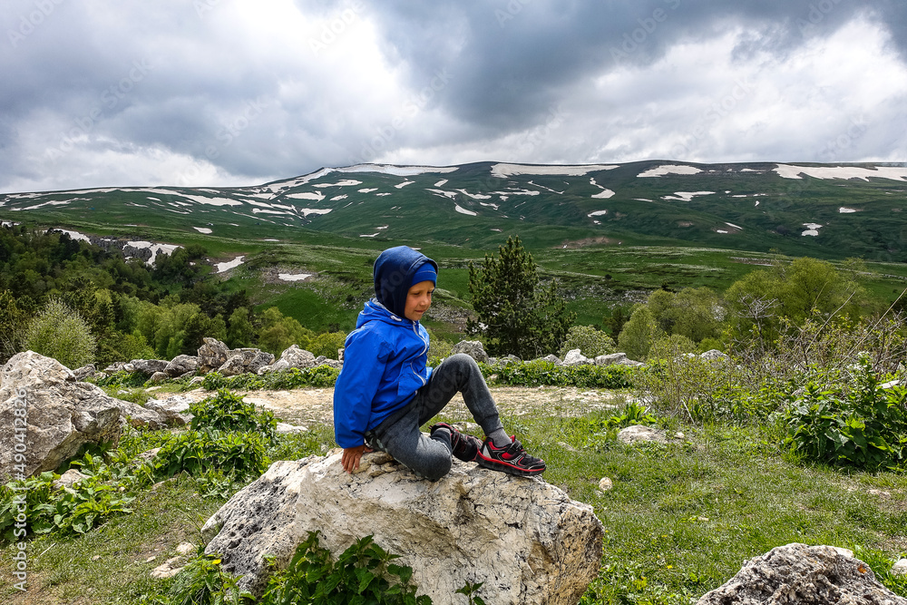 A little boy on the background of the alpine meadows of the Lago-Naki plateau in Adygea. Russia. 2021.