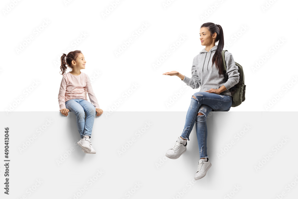 Female student sitting on a blank panel and talking to a little girl