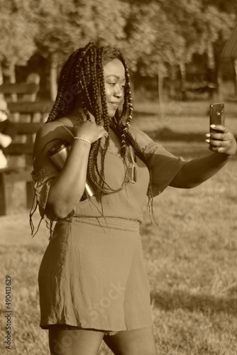 A young african pretty girl from Cameroon with a mobile phone. A dark-skinned girl in a dress takes pictures of herself on a mobile phone on the street. Black and white photo.