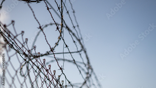 Barbed wire against cloudy blue sky.