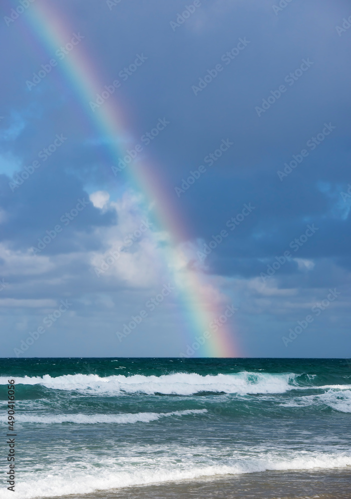 Rainbow shining in stormy sky as waves roll onto shore Rainbow shining in stormy sky as waves roll onto shore