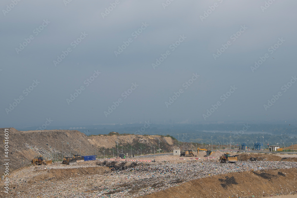 Dump trucks unloading garbage over vast landfill. Environmental pollution. Waste disposal. Work of special equipment and bulldozer machines clearing up garbage. Seagulls over the landfill.