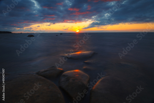 Rocky shore with stones sinking in the sea water. Sunset, long exposure. Baltic sea.
