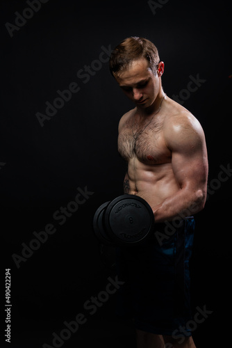 Man on black background keeps dumbbells pumped up in fitness biceps athlete weight fitness powerful, shirtless lifestyle. Young sportive guy fit