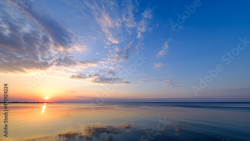 Beautiful, colorful sunset, sunrise over a wide river. Twilight rays and clouds reflected in the calm water.
