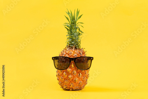 Ripe pineapple with sunglasses on yellow background