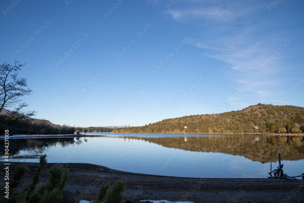 View of the peaceful lake in a summer sunny day. The forest, mountains and blue sky reflection in the water surface. 
