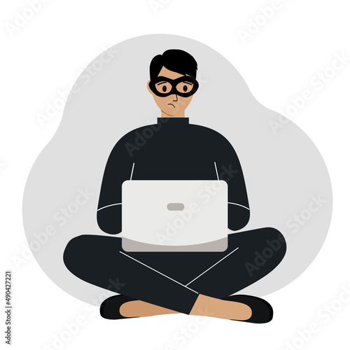 Hacker in a black mask with a computer. The cybercriminal is holding a laptop. Cyber attack, mobile phishing, scam.