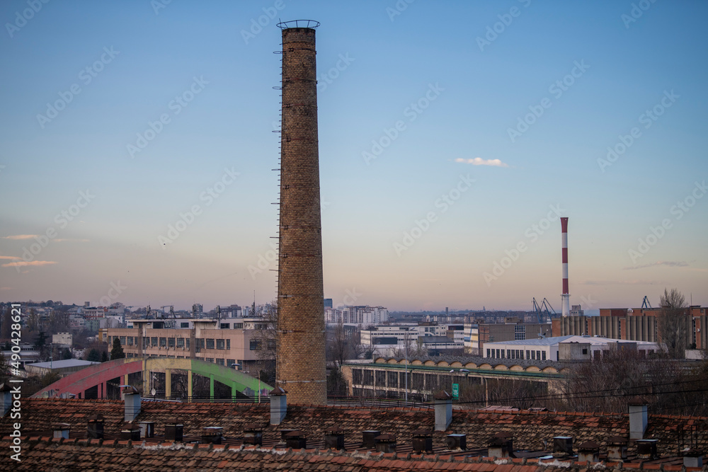 Defunct industrial brick chimney with beautiful cityview in background at sunset. Ecology and industrial renewal concept.