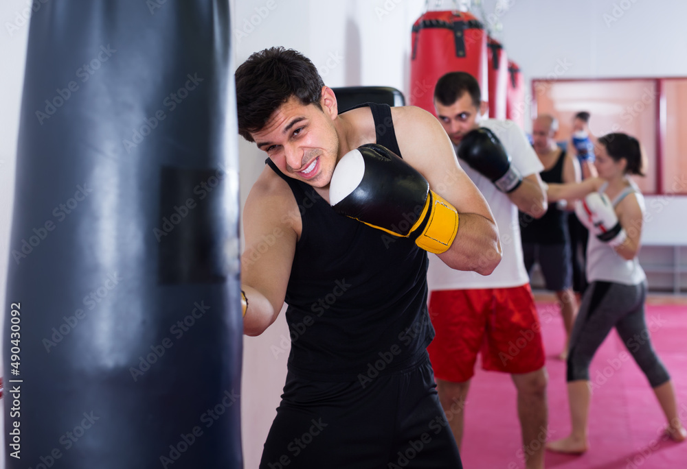 strenuous sportsman in the boxing hall practicing boxing punches with boxing bag during training