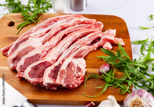 Raw lamb chops on wooden cutting board with garlic and herbs, over white background.