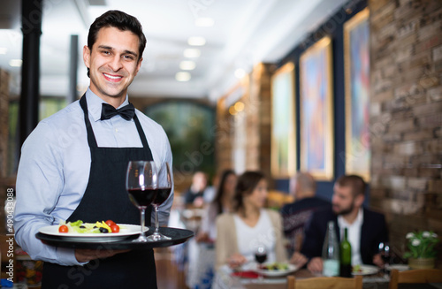 Professional smiling pleasant waiter holding serving tray for restaurant guests