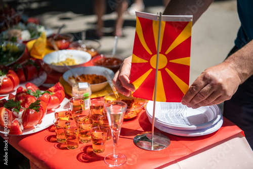 Breakfast buffet with various traditional North Macedonian food and alcohol drinks. Hands holding North Macedonian national flag. photo