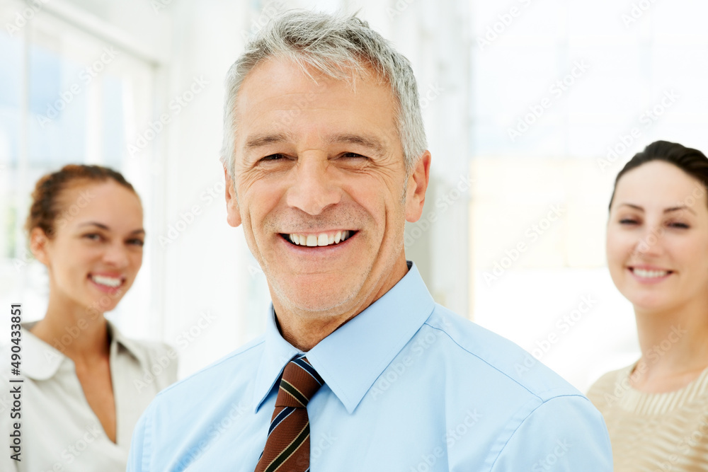 Smiling senior businessman with colleagues at the back. Portrait of smiling senior businessman with colleagues in the background. Smiling senior businessman with colleagues at the back. Portrait of smiling senior businessman with colleagues in the background.