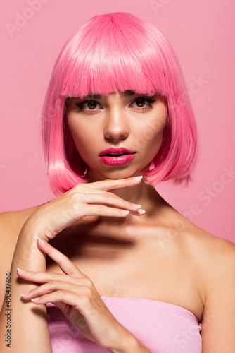 young woman with colored hair and bangs looking at camera isolated on pink.