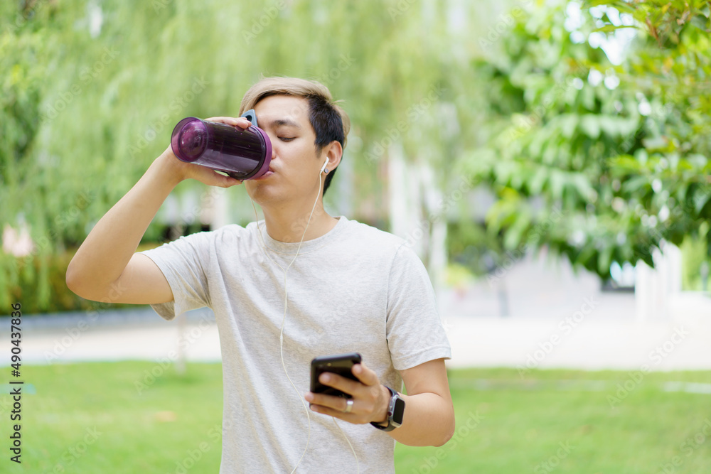 Handsome Asian young sportsman posing and smiling to the camera while drinking water. Handsome Asian young sportsman posing and smiling to the camera while drinking water.