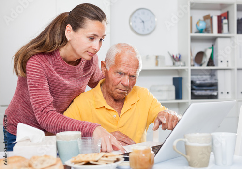Portrait of mature man working at laptop, daughter trying to help him