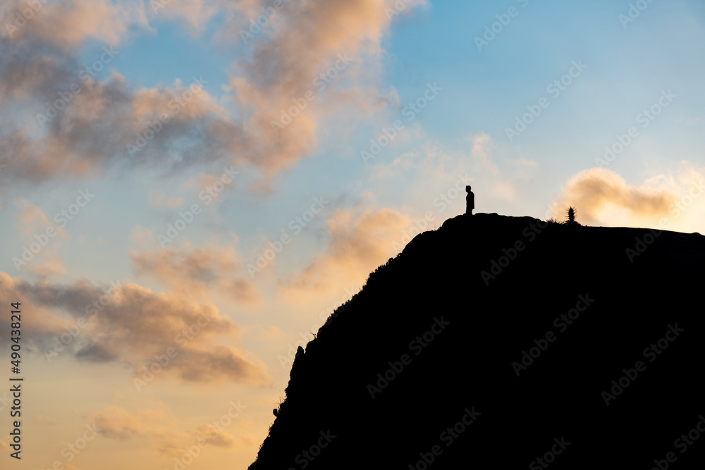 Silhouette of a man looking towards the horizon from a cliff in a sunset