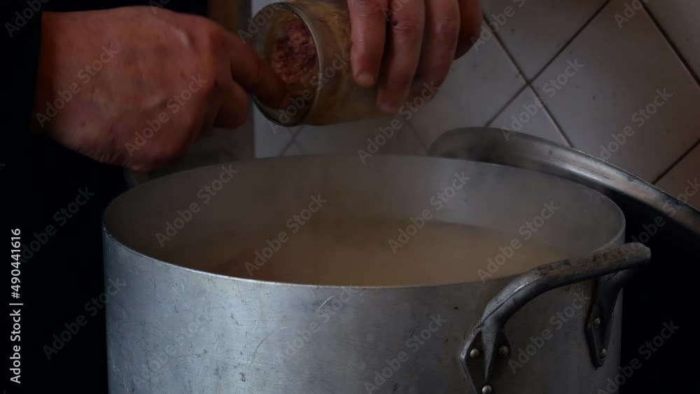 A volunteer cook adds pork stew to a large pot while preparing food for the homeless. A volunteer cook prepares lunch for a group of refugees. A volunteer cook adds pork stew to a large pot while preparing food for the homeless. A volunteer cook prepares lunch for a group of refugees.