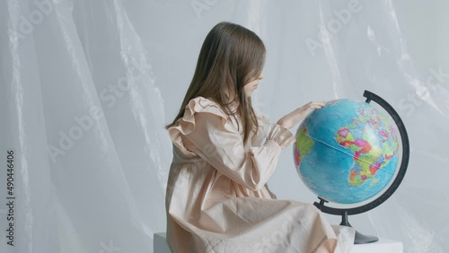 A teen girl sits on a white cube and spins the globus