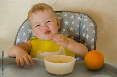 A little baby eats an orange at a children's table