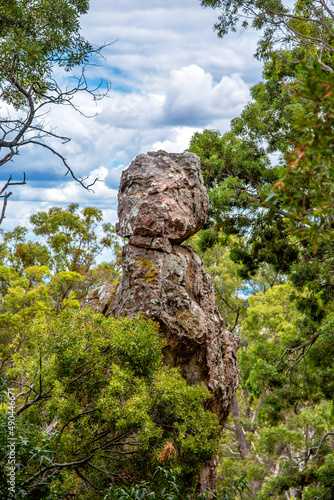 A volcanic boulder emerges from the bushland at Hanging Rock in Victoria, Australia, with white fluffy clouds in the distance photo