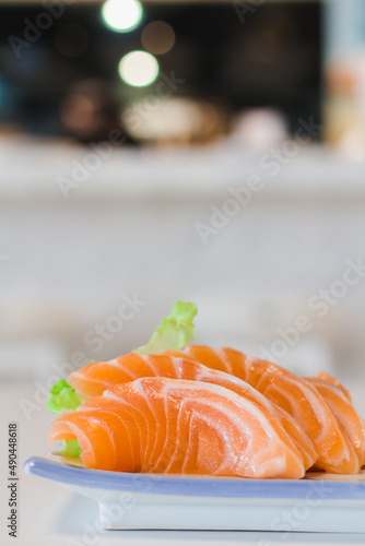Lateral view or side of raw salmon sashimi slices, Japanese food style, on white and blue ceramic plate and white table background.