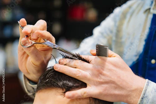 Obraz hairdresser makes a haircut for a brunet man with a scissors in a barbershop