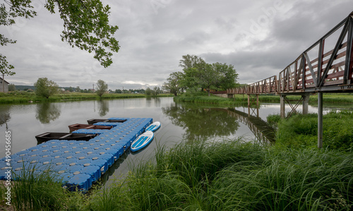 Pontoon floating moorings for boats located on the river. A pair of stand up paddle board standing at the pier. Summer cloudy landscape of the middle lane.