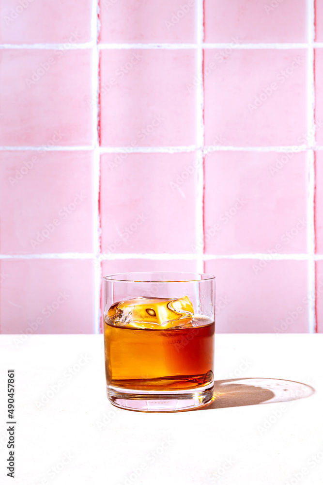 Whiskey or bourbon in a rocks glass with a big ice cube, shot with hard  light and harsh shadows, pink tile backdrop, copy space Stock Photo