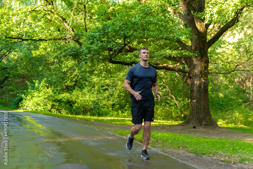 A man athlete runs in the park outdoors, around the forest, oak trees green enduring athletic athlete run athlete lifestyle fit wellness jog, park outside. Autumn leisure spring, runners stretches