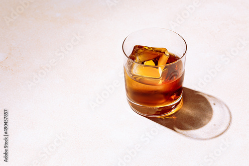 Whiskey or bourbon in a rocks glass with a big ice cube, shot with hard light and harsh shadows, bright backdrop, copy space