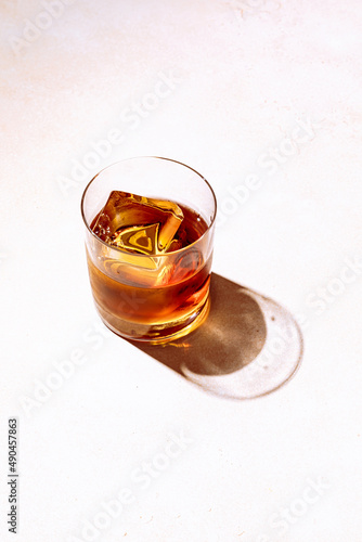 Whiskey or bourbon in a rocks glass with a big ice cube, shot with hard light and harsh shadows, bright backdrop, copy space