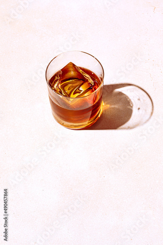 Whiskey or bourbon in a rocks glass with a big ice cube, shot with hard light and harsh shadows, bright backdrop, copy space