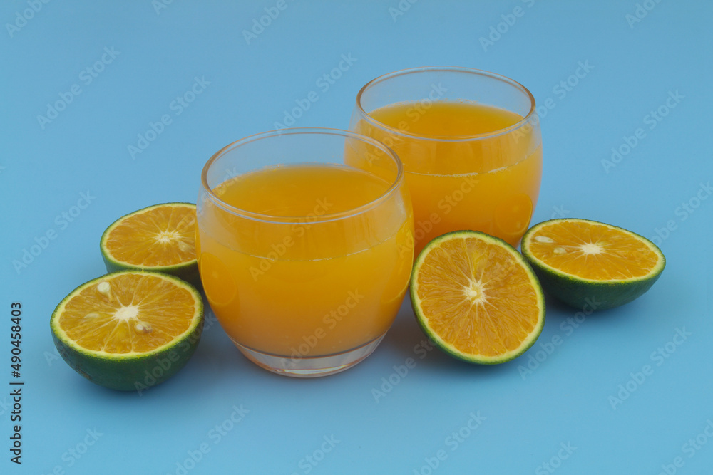 Glasses of fresh orange juice and green orange fruits on blue background Glasses of fresh orange juice and green orange fruits on blue background