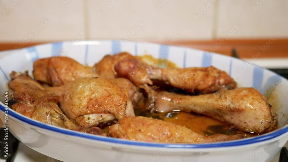 Woman Lays Out Cooked Roast Chicken Legs from a Heat-Resistant form with Forceps. Barbecue of fried chicken drumsticks with a crispy crust in the home kitchen. Drops of fat dripping into a plate. 4K. Woman Lays Out Cooked Roast Chicken Legs from a Heat-Resistant form with Forceps. Barbecue of fried chicken drumsticks with a crispy crust in the home kitchen. Drops of fat dripping into a plate. 4K.