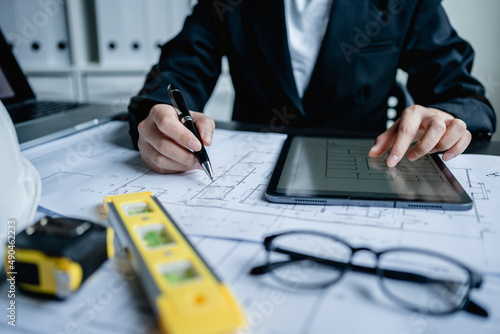 Close up of businesswomen or female engineer using digital tablet working with drawing draft Blueprint on the desk, Architectural project, Real Estate, Architecture and Construction Concept.