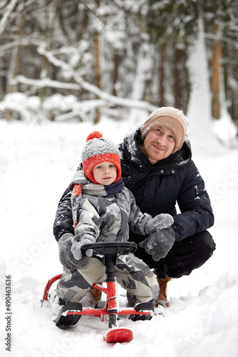 Father and his son in funny hat having fun and laughing in snowy winter forest. Happy family wearing warm winter clothes enjoying wintertime in snow covered pine forest. Outdoor activities with kids.